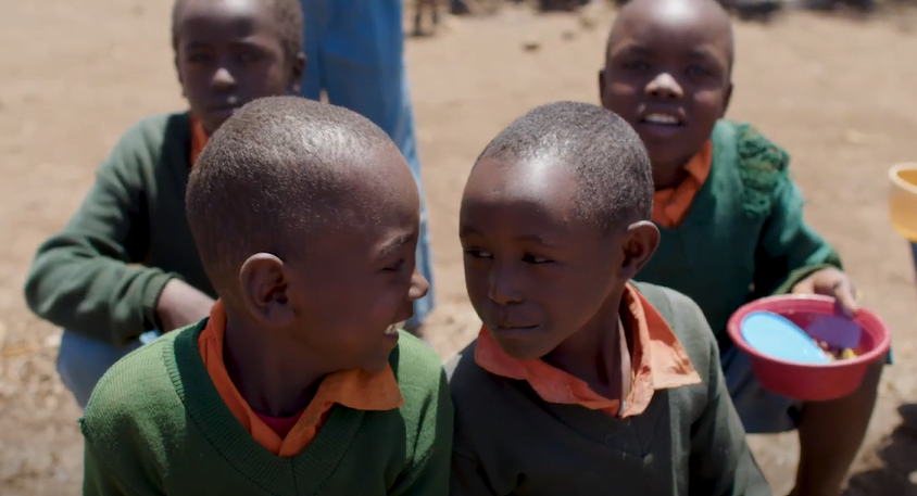 Children looking at each other smiling while two others are in the background looking at the camera while smiling